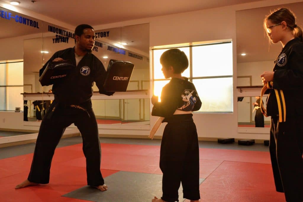 youth student practicing hitting training target pads being held by instructor